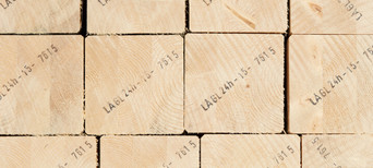 Gestapelte Brettschichtholzbalken mit sichtbarer Jahresringstruktur und Markierungen für den Holzbau.